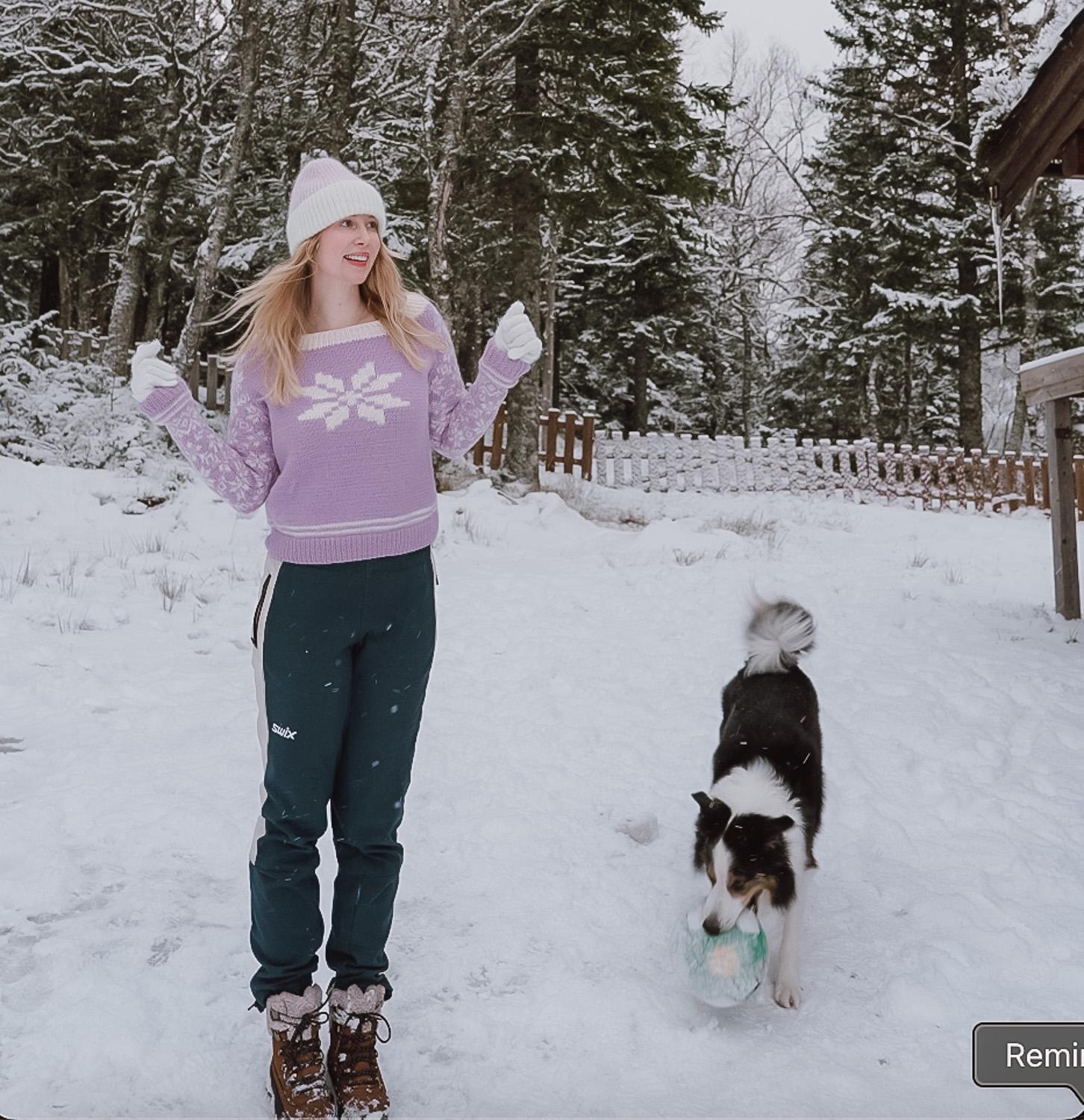 woman wearing a purple snowflake sweater standing next to her dog